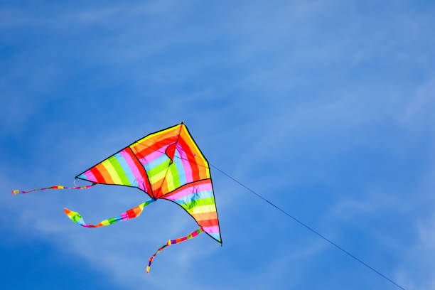 istock rainbow colored kite flying high in the blue sky with some white clouds 1448166450