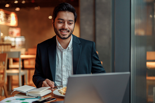 Handsome indian businessman working on laptop in cozy cafe sitting near window. High quality photo