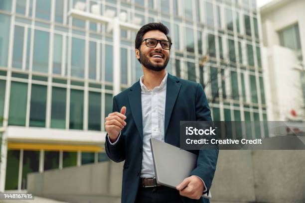 Smiling Indian Businessman In Suit And Glasses With Laptop Near Office Building Stock Photo - Download Image Now