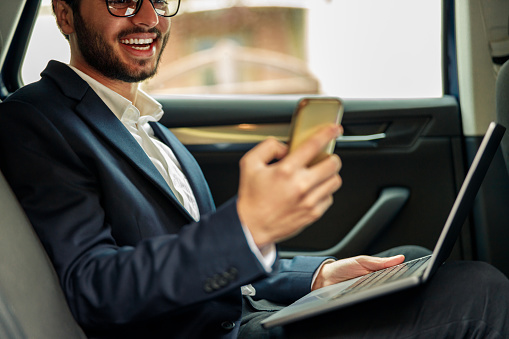 Smiling businessman in suit working laptop while riding in car to office. High quality photo