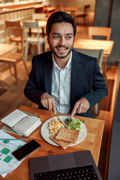 Indian businessman eating lunch during break after work in cafe and looking at side stock photo
