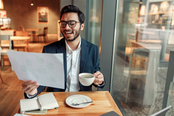 istock Smiling indian businessman drinking coffee and working with documents in cafe 1448168996