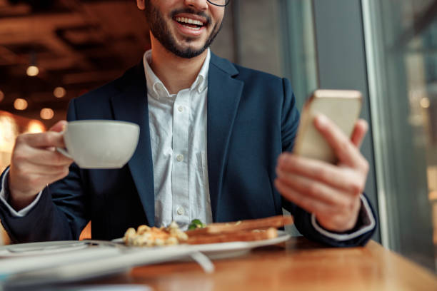 istock Smiling Indian businessman wearing suit is using phone during lunch time in cafe. Blurred background 1448169214