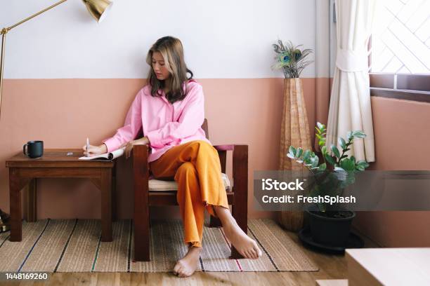A Serious Beautiful Businesswoman In Pink Shirt And Orange Trousers Taking Notes While Relaxing At Home Stock Photo - Download Image Now