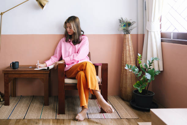 a serious beautiful businesswoman in pink shirt and orange trousers taking notes while relaxing at home - education relaxation women home interior imagens e fotografias de stock