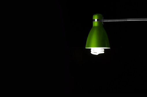 Detail of green desk lamp on black background, with light bulb. Copy space. Horizontal orientation. No people.