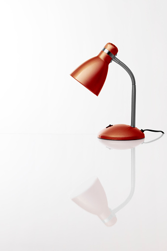 Red desk lamp on light background, with reflection on the table. Copy space. Vertical orientation. No people.