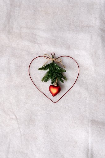 On a white background with imitation snow texture, an advent wreath. The crown is heart-shaped and in the center next to a green branch a small red heart.