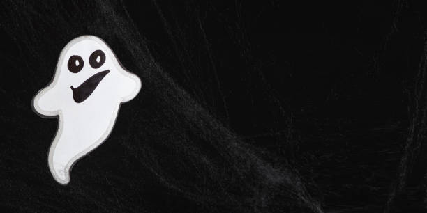 istock A cheerful white ghost with a face smiles and flies on a black background with a web, banner with place for text 1448181121