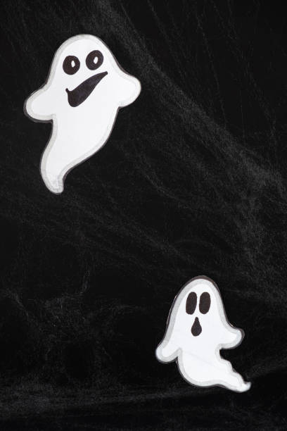 istock Two merry ghosts with faces fly and smile on a black background with a web. Halloween card, a place for text 1448181124