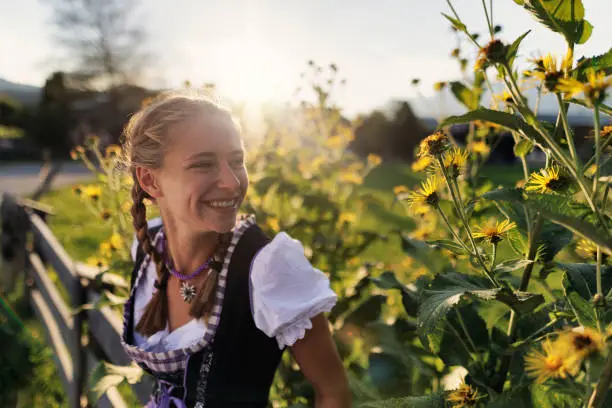 Teenage girl wearing Austrian and south German traditional dress - Dirndl.
The girl is enjoying idyllic flowers and sunset in the the Austrian village.
Sunny summer day.
Canon R5