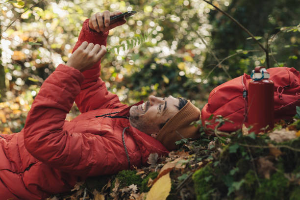 istock young adult caucasian man in red coat and red backpack smiling happily while using his mobile phone in a forest in nature during a hiking trip. 1448185226
