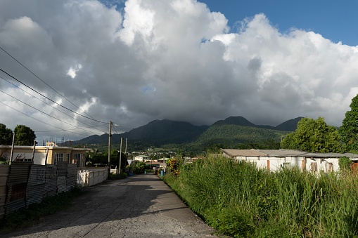 Road and houses in a town or village in Dominica with hills in the background on a cloudy day