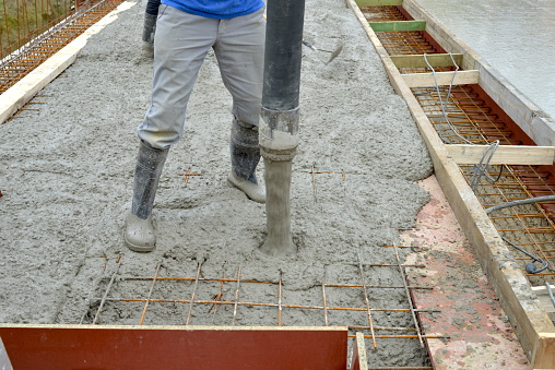 Building cement floor construction works. Construction site worker holding a cement pipe and controlling the concrete fluid flowing on the floor from the cement truck between steel bars mesh