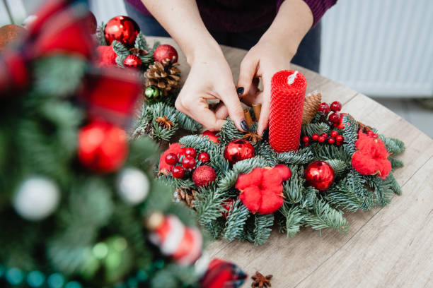 istock A woman decorator makes a Christmas decorative stand from spruce branches, a red wax candle, red cotton twigs and red Christmas balls at a wooden round table. There are only hands in the frame 1448196391
