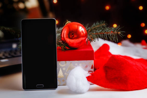 istock a black smartphone standing vertically next to a gift box, a red Christmas ball and a red Santa Claus hat. Christmas gifts 1448196963