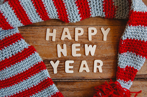 Inscription of white wooden letters Happy New Year on a wooden background with striped knitted hat