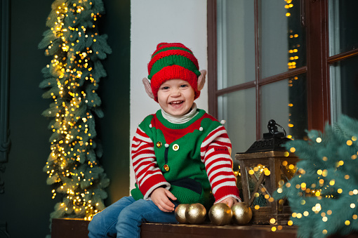 Toddler boy in elf costume for Christmas on windowsill.