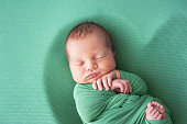 Newborn baby in green diaper is sleeping.
