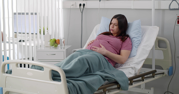 Pregnant woman lying in patient bed having stomach aches. Pregnant woman in delivery room having contractions preparing for giving birth in hospital
