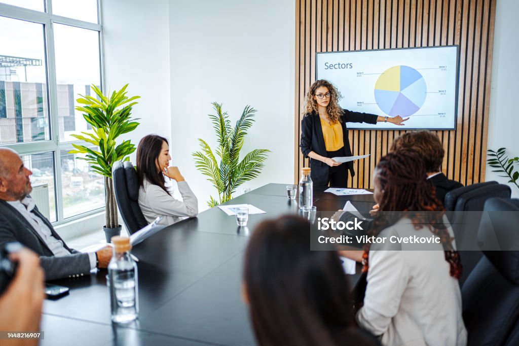 Businesswoman leading business meeting using statistics chart on presentation TV Presentation - Speech Stock Photo