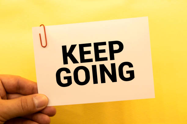 On a light pink background - a craft envelope. It has a white sheet of paper that says KEEP GOING. stock photo