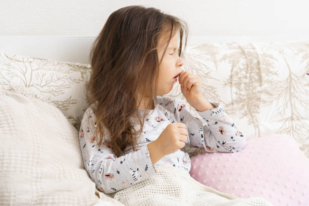 Poor, unfortunate little brunette preschooler child, girl in pajamas coughing, lying in soft bed. Sore throat, angina Poor, unfortunate little brunette preschooler child, girl in pajamas coughing, lying in soft bed. Sore throat, angina, tonsillitis. Recovering, health care, home treatment and bed rest. Copy space coughing stock pictures, royalty-free photos & images