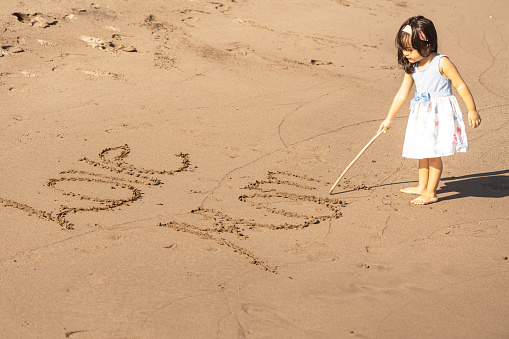 Little girl writing I love you mom in the sand on a beach