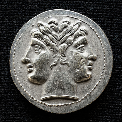 Ancient coin showing two-headed Roman god Janus, 225-214 BC. Old rare money, silver didrachm isolated on dark background, macro. Concept of Rome, valuable coin, past civilization and history.