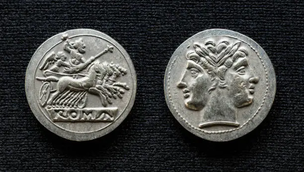 Ancient Roman coin showing Jupiter on horses and god Janus, 225-214 BC. Old rare money, silver didrachm isolated on dark background, macro. Concept of Rome, valuable coin, civilization and history.