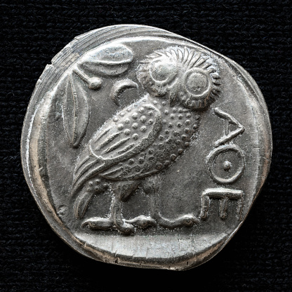 Ancient Greek coin showing owl and inscription Athens. Old rare money, silver tetradrachm isolated on dark background, macro. Concept of Greece, valuable coin, past civilization, artifact and history