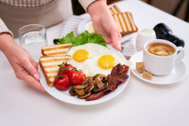 istock Fried eggs, bacon, tomato, toasted bread in white ceramic plate and cup of coffee 1448225576