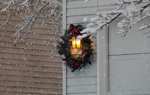 A holiday winter Christmas wreath hung on a light outside a home.