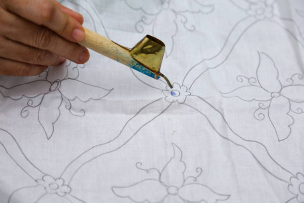 istock Batik craftsmen's hands hold a canting and paint batik on a white cloth 1448229385