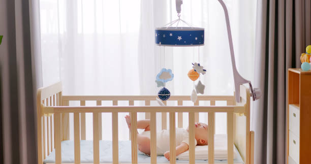 Cute newborn baby in crib at home and he is watching toys which hanging above cot