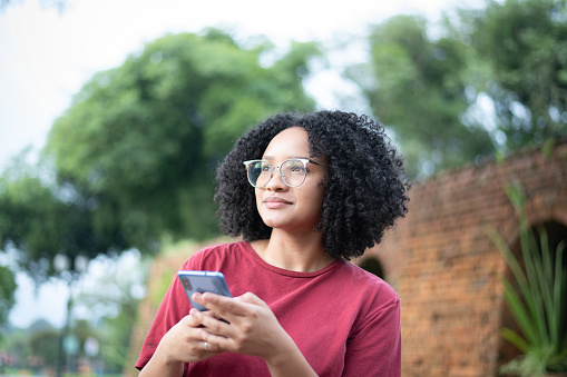 Environmental portrait of a beautiful young black woman looking away as she thinks of what to text in mobile phone message