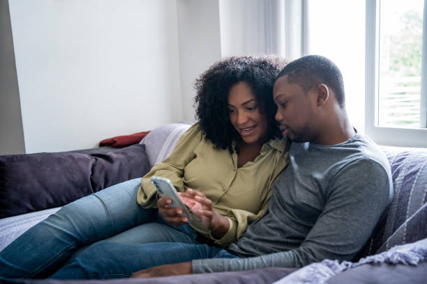 istock Black couple sitting on sofa watching video on cell phone 1448239696