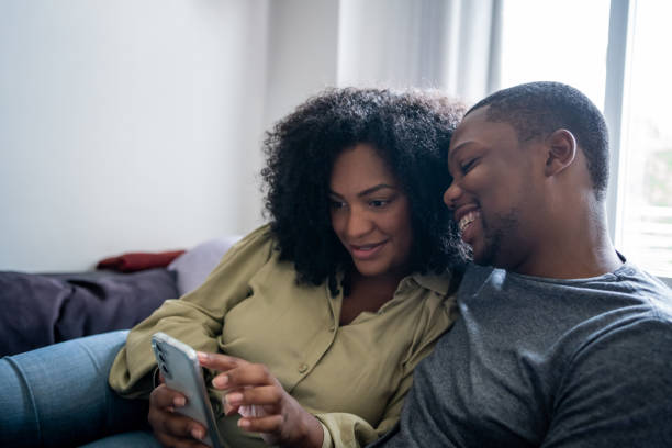 istock Black couple sitting on sofa watching video on cell phone 1448239697