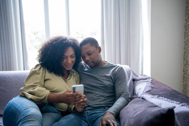 istock Black couple sitting on sofa watching video on cell phone 1448239698