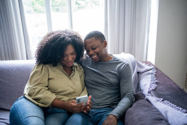 istock Black couple sitting on sofa watching video on cell phone 1448239702