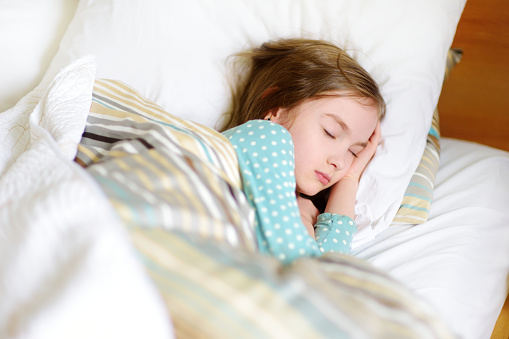 Adorable little girl sleeping in the bed. Tired child taking a nap under white blanket. Bedtime for kids.