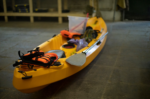 Yellow boat made of plastic. Canoe in garage. Sports equipment. Preparation for hike. Boat and paddle.