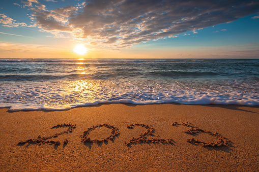 Ocean beach sunrise and text Happy new year 2023 on coast sand. Sea sunset.