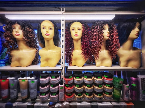 Plastic female mannequin heads in a row wearing different wigs illuminated in a shop window.