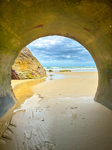 Looking out from a tunnel at the beach to a seagull and the cloudy sky.