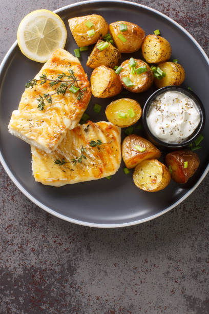 Healthy dinner of grilled white fish with baked potatoes close-up in a plate. Vertical top view stock photo