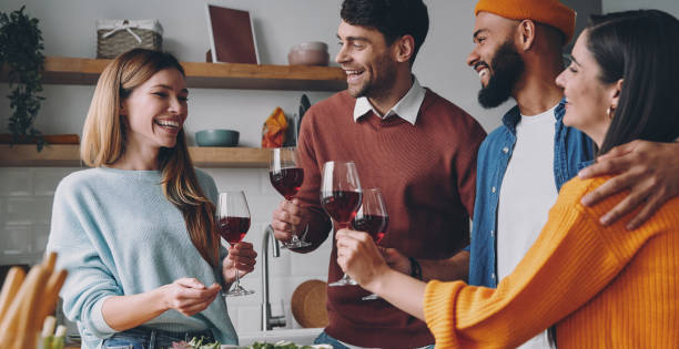Group of beautiful young people talking and smiling while enjoying dinner at home together stock photo