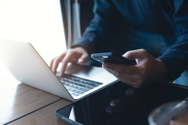istock Young man sitting in coffee shop, using mobile phone browsing internet with laptop computer and digital tablet on table, male freelancer working at cafe 1448288759