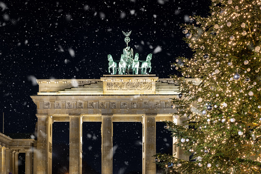 The famous Brandeburg Gate in Berlin, Germany, during winter night time with lit christmas tree and snow falling