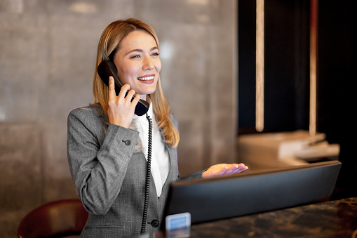 Smiling receptionist taking a telephone call while standing behind the counter in a hotel lobby